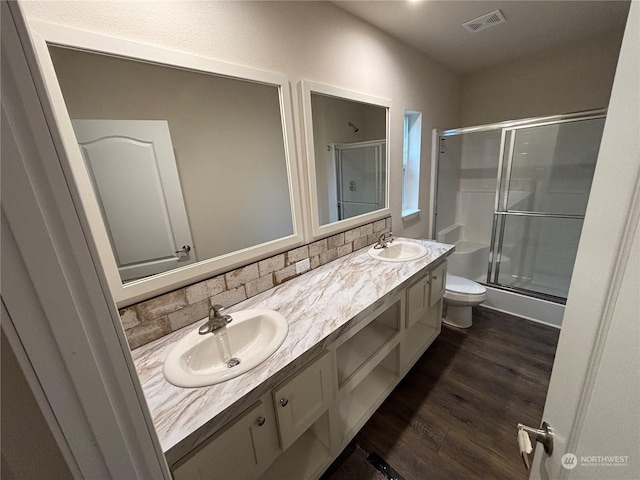 bathroom with wood-type flooring, toilet, decorative backsplash, a shower with door, and vanity