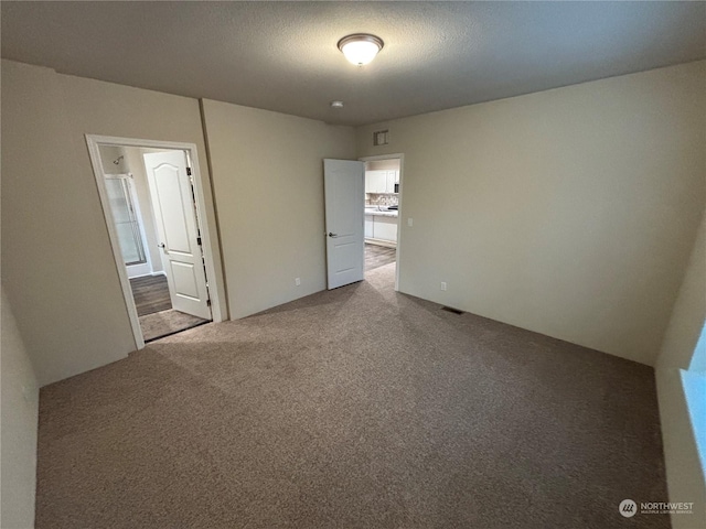 unfurnished bedroom featuring a textured ceiling, carpet floors, connected bathroom, and visible vents