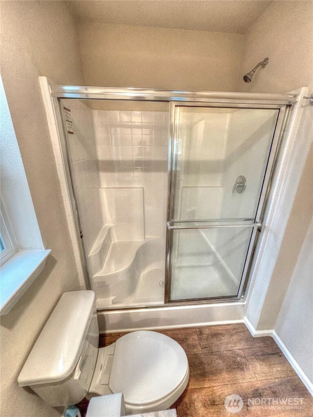 full bathroom with wood finished floors, a shower stall, toilet, and baseboards