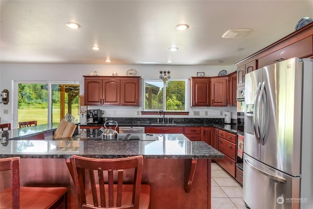 kitchen featuring stainless steel fridge, dark stone counters, a breakfast bar, sink, and light tile patterned flooring