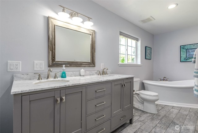 bathroom featuring wood-type flooring, vanity, a tub to relax in, and toilet