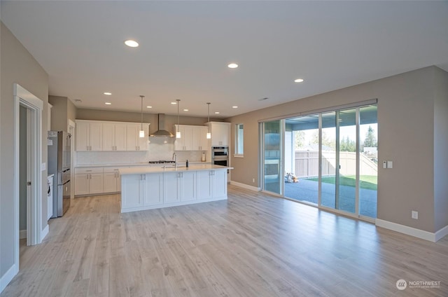 kitchen with white cabinetry, wall chimney range hood, pendant lighting, and a kitchen island with sink