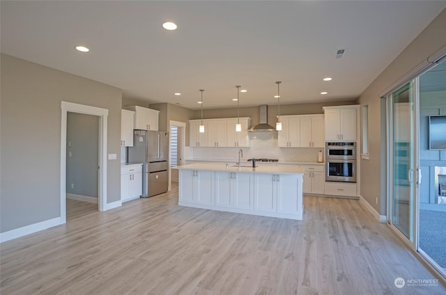 kitchen with pendant lighting, sink, stainless steel appliances, white cabinets, and wall chimney exhaust hood