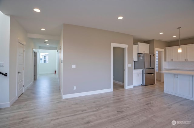 kitchen with white cabinetry, stainless steel fridge, decorative light fixtures, and light hardwood / wood-style flooring