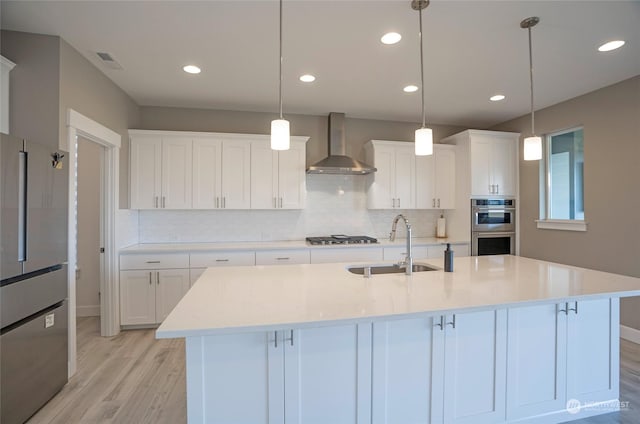 kitchen with an island with sink, decorative light fixtures, white cabinets, and wall chimney exhaust hood