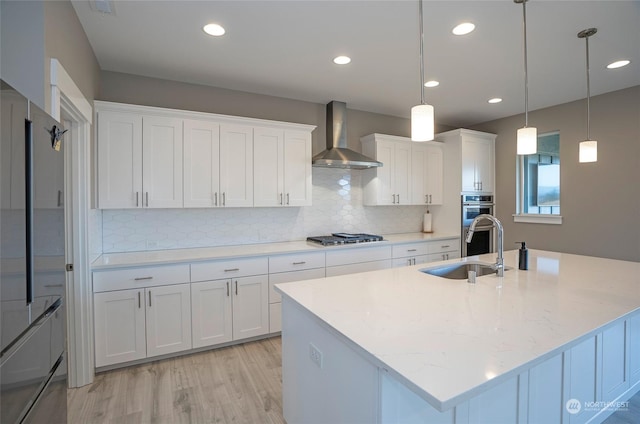 kitchen with pendant lighting, white cabinetry, sink, stainless steel appliances, and wall chimney range hood