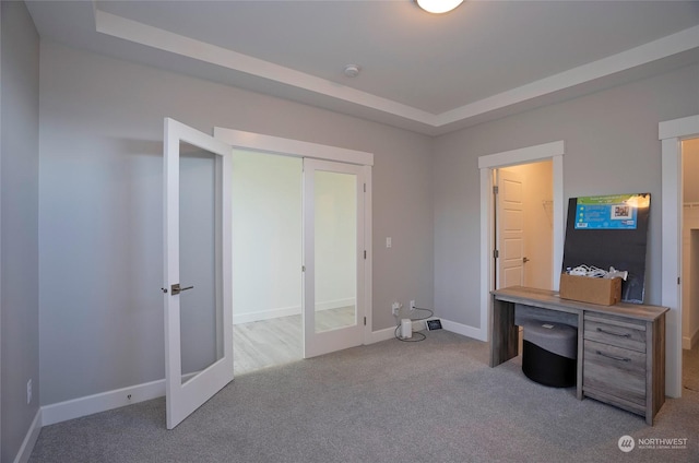 carpeted home office with french doors and a tray ceiling