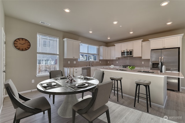 kitchen featuring white cabinets, decorative backsplash, light wood-type flooring, a kitchen island, and stainless steel appliances