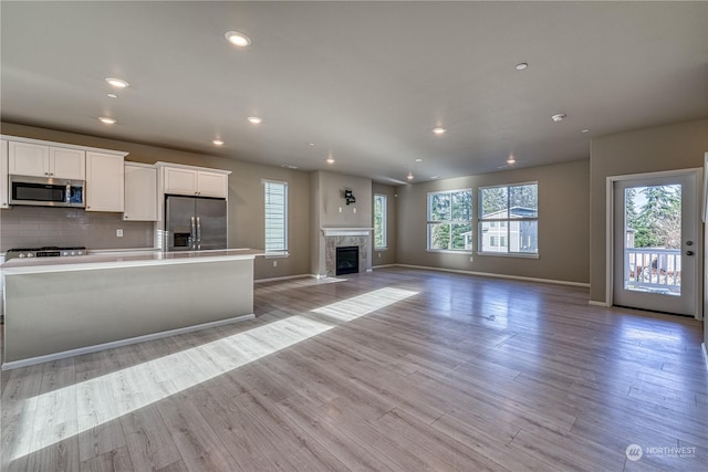 kitchen featuring a tile fireplace, stainless steel appliances, light hardwood / wood-style flooring, and white cabinetry