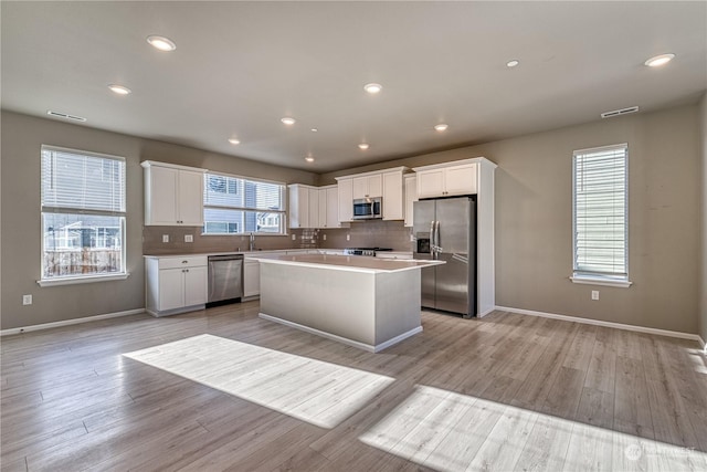 kitchen featuring decorative backsplash, light wood-type flooring, stainless steel appliances, white cabinets, and a kitchen island