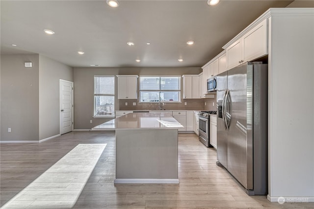 kitchen with a center island, stainless steel appliances, backsplash, white cabinets, and light wood-type flooring