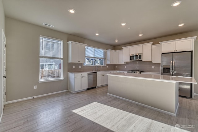 kitchen featuring decorative backsplash, appliances with stainless steel finishes, light wood-type flooring, a center island, and white cabinetry