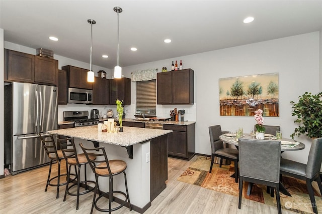 kitchen featuring dark brown cabinetry, stainless steel appliances, pendant lighting, light hardwood / wood-style floors, and a center island with sink