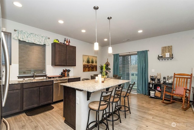 kitchen with appliances with stainless steel finishes, light stone counters, sink, a kitchen island, and hanging light fixtures