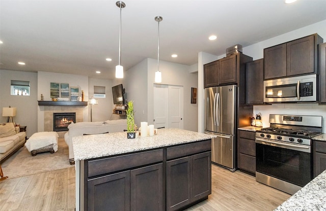 kitchen with appliances with stainless steel finishes, light stone counters, dark brown cabinets, decorative light fixtures, and light hardwood / wood-style floors