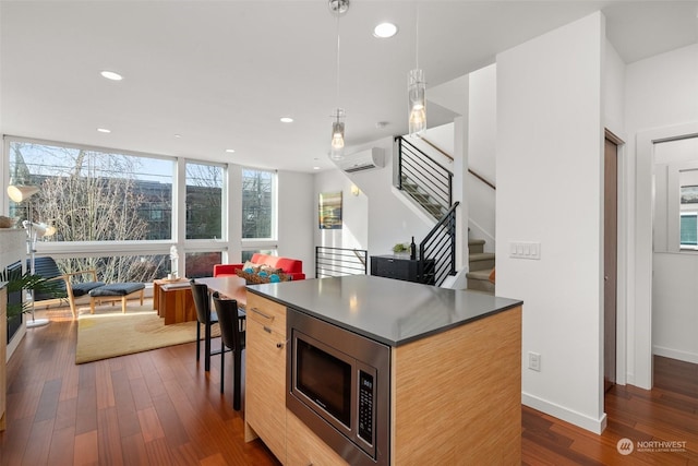 kitchen with pendant lighting, stainless steel microwave, dark wood-type flooring, a kitchen island, and a wall unit AC