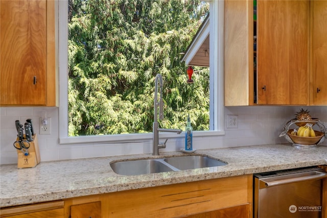 kitchen with sink, stainless steel dishwasher, a healthy amount of sunlight, and light stone counters