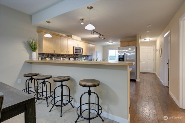 kitchen featuring hardwood / wood-style floors, hanging light fixtures, light brown cabinetry, kitchen peninsula, and stainless steel appliances