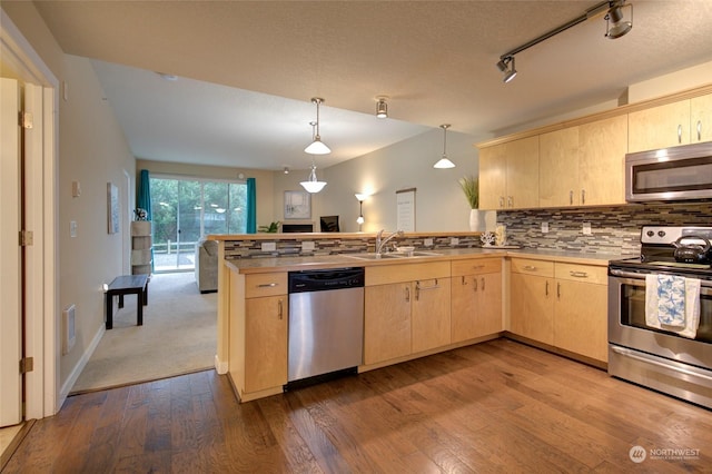 kitchen featuring kitchen peninsula, appliances with stainless steel finishes, light brown cabinets, wood-type flooring, and decorative light fixtures