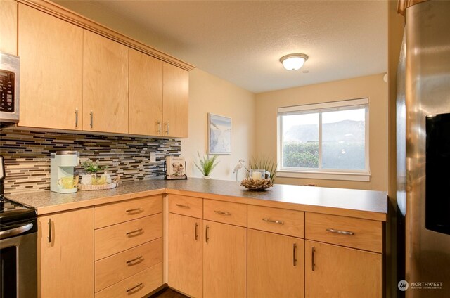 kitchen featuring kitchen peninsula, backsplash, a textured ceiling, stainless steel appliances, and light brown cabinets