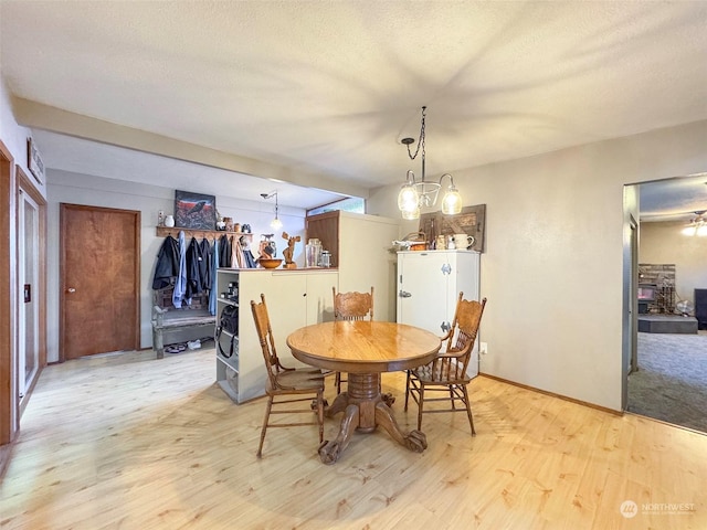 dining area with a textured ceiling, light wood-type flooring, and a notable chandelier