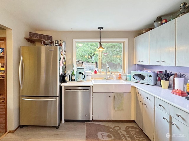 kitchen featuring white cabinetry, sink, stainless steel appliances, pendant lighting, and light wood-type flooring