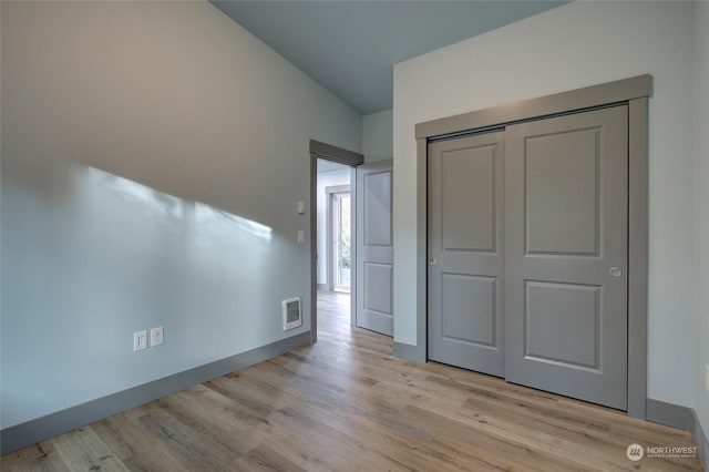 unfurnished bedroom featuring lofted ceiling, a closet, and light wood-type flooring