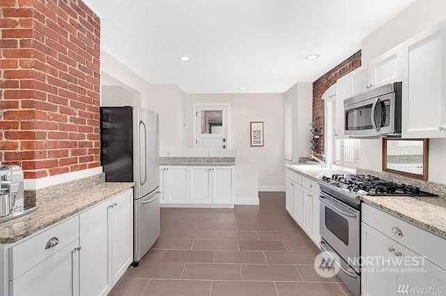 kitchen featuring light stone counters, stainless steel appliances, dark tile patterned floors, white cabinetry, and sink