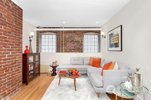 living room featuring brick wall, light wood-type flooring, and radiator heating unit