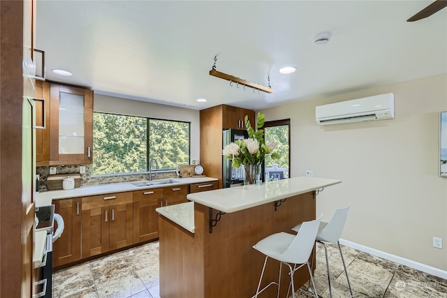 kitchen with sink, tasteful backsplash, a wall unit AC, a breakfast bar area, and a kitchen island