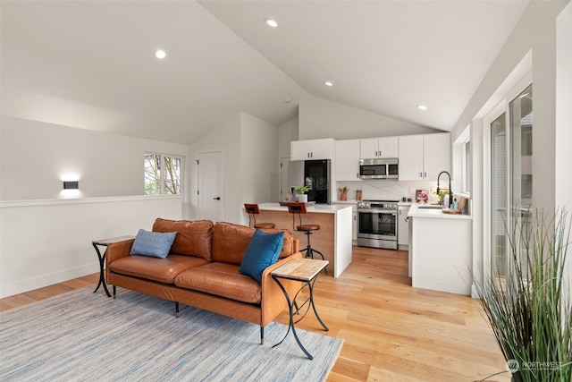 living room with light hardwood / wood-style floors, vaulted ceiling, and sink