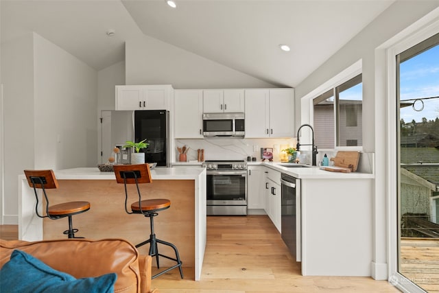 kitchen with sink, light hardwood / wood-style floors, a kitchen bar, white cabinetry, and stainless steel appliances