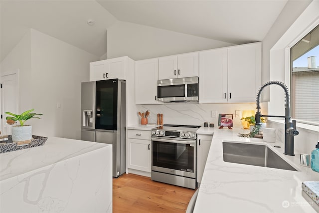 kitchen with white cabinets, sink, light hardwood / wood-style flooring, vaulted ceiling, and appliances with stainless steel finishes