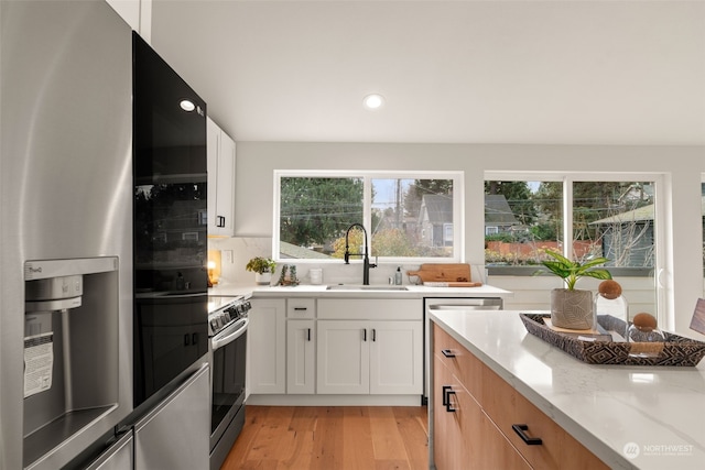 kitchen featuring light stone countertops, white cabinetry, black fridge, and sink