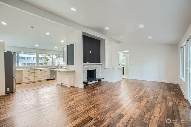 unfurnished living room featuring built in desk, light wood-type flooring, a fireplace, and vaulted ceiling