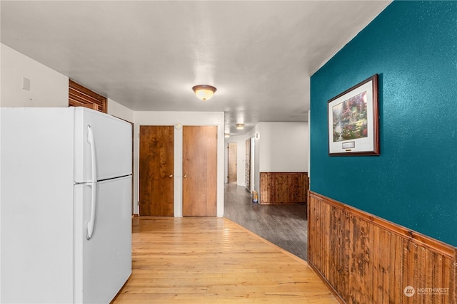 kitchen featuring white refrigerator, light hardwood / wood-style flooring, and wooden walls