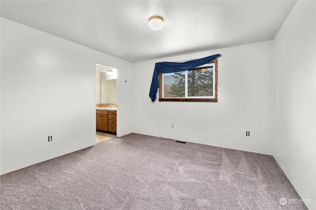 unfurnished bedroom featuring ensuite bathroom and light carpet