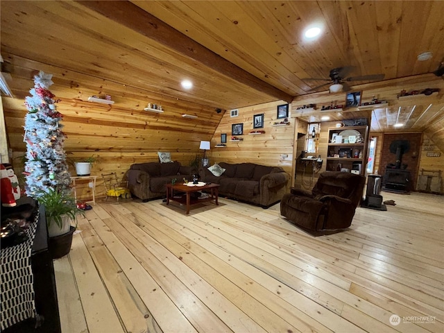 living room featuring wood walls, wooden ceiling, a wood stove, ceiling fan, and light hardwood / wood-style floors