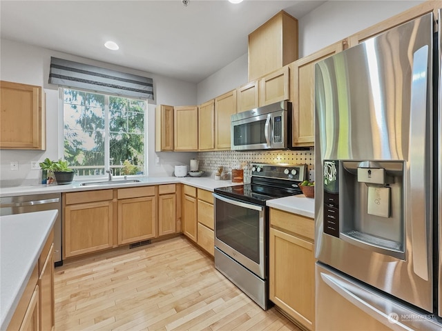 kitchen with appliances with stainless steel finishes, light hardwood / wood-style flooring, light brown cabinets, and sink