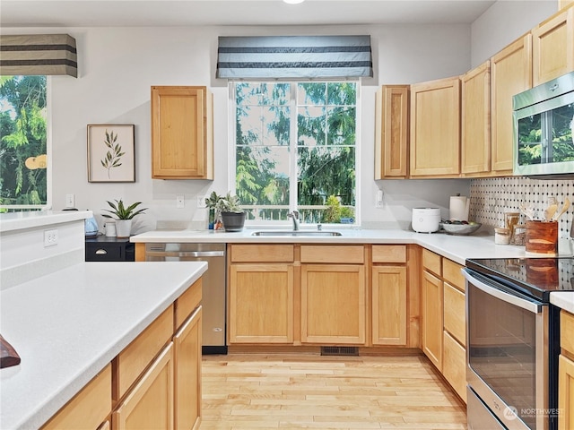 kitchen with sink, light brown cabinets, light wood-type flooring, and appliances with stainless steel finishes