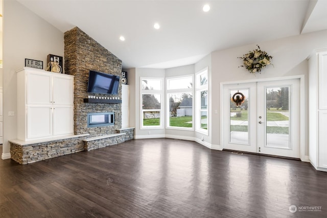 unfurnished living room featuring dark hardwood / wood-style floors, vaulted ceiling, a stone fireplace, and french doors