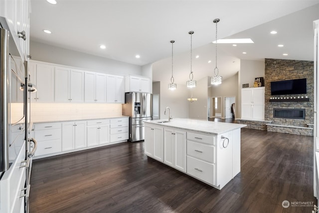 kitchen featuring stainless steel refrigerator with ice dispenser, sink, a center island with sink, white cabinetry, and hanging light fixtures