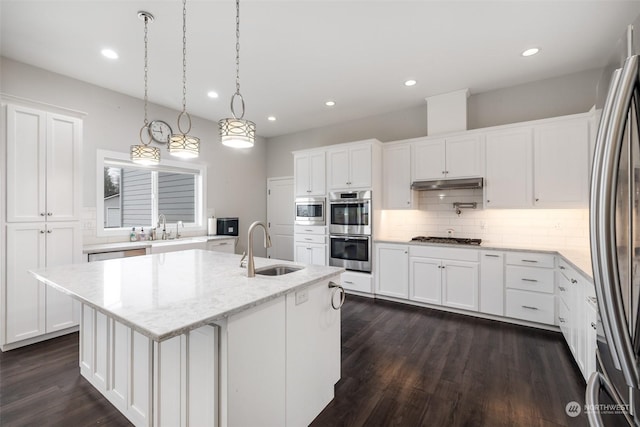 kitchen featuring stainless steel appliances, sink, decorative light fixtures, a center island with sink, and white cabinets