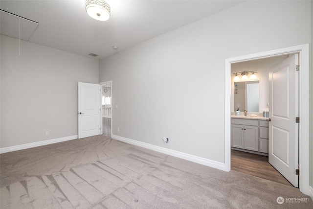 unfurnished bedroom featuring sink, light carpet, and ensuite bath