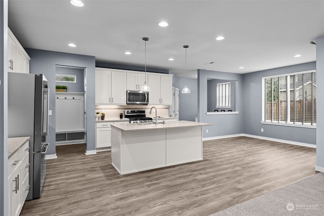 kitchen featuring appliances with stainless steel finishes, sink, decorative light fixtures, white cabinetry, and an island with sink