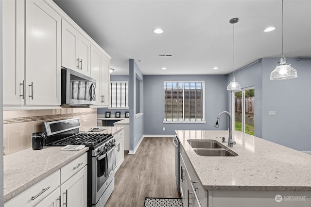 kitchen with sink, hanging light fixtures, stainless steel appliances, a center island with sink, and white cabinets