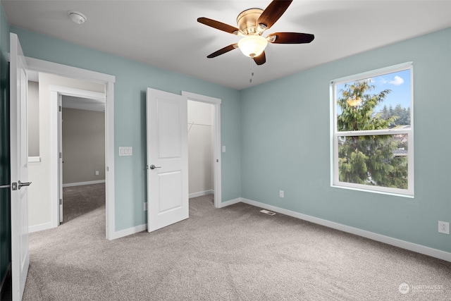 unfurnished bedroom with a walk in closet, a closet, light colored carpet, and ceiling fan