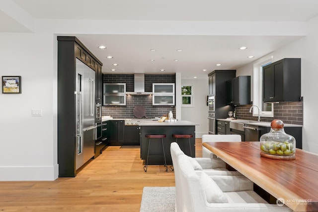 kitchen featuring a kitchen island, backsplash, light wood-type flooring, and wall chimney range hood