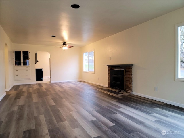 unfurnished living room featuring ceiling fan, dark hardwood / wood-style flooring, and a brick fireplace