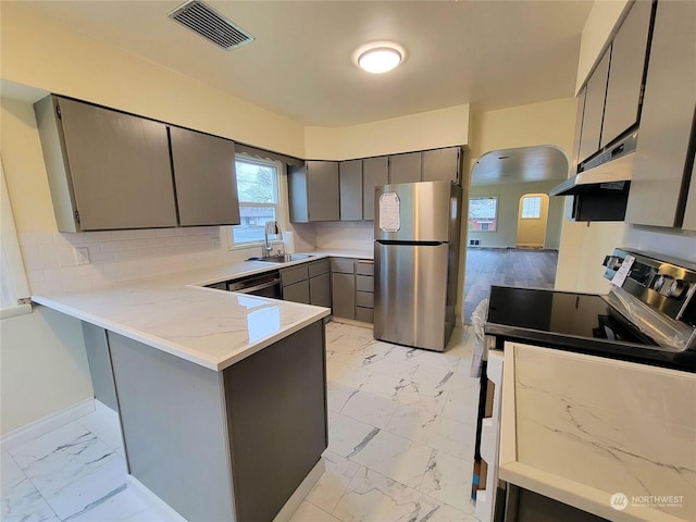 kitchen featuring sink, gray cabinets, range hood, appliances with stainless steel finishes, and kitchen peninsula